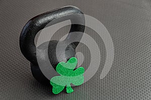 Black iron kettlebell with green shamrock on a black gym floor, holiday fitness