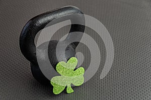 Black iron kettlebell with green shamrock on a black gym floor, holiday fitness