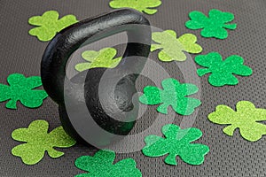 Black iron kettlebell with green shamrocks on a black gym floor, holiday fitness