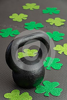 Black iron kettlebell with green shamrocks on a black gym floor, holiday fitness