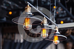 Black iron loft chandeliers with edison lamps on a black background, bokeh. Concept of modern interior design of restaurant, cafe