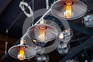 Black iron loft chandeliers with edison lamps on a black background, bokeh. Concept of modern interior design of restaurant, cafe