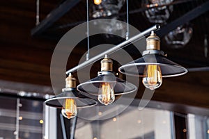 Black iron loft chandeliers with edison lamps on a black background, bokeh. Concept of modern interior design of restaurant, cafe