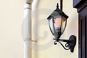 Black iron wall lantern in retro style with glass shade and electric light bulb.