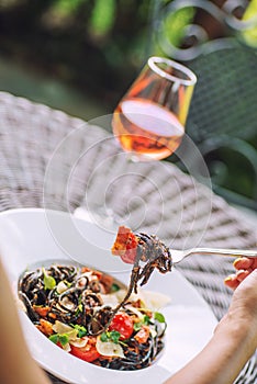 Black italian pasta with tomato sauce and parmesan, served on white plate with glass of wine, product photography for restaurant