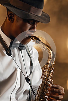 Black jazzman in hat plays the saxophone on stage