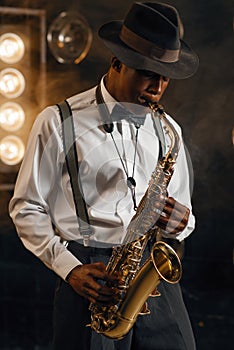 Black jazzman in hat plays the saxophone on stage