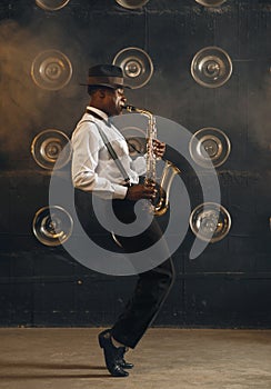 Black jazzman in hat plays the saxophone on stage