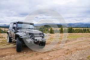 Black jeep parked in carpathians with picturesque mountain forests and clouds panorama