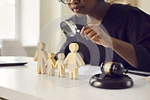 Judge with magnifying glass looking at little family figures standing on her table photo