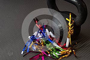 Black kettlebell on a black gym floor with blue, green, red, pink and gold noisemakers