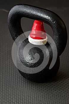 Black kettlebell on a black gym floor with small red and white Santa Claus hat