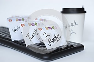 On the black keyboard many stickers with the names of the days of the week. next to a paper Cup of coffee with the inscription