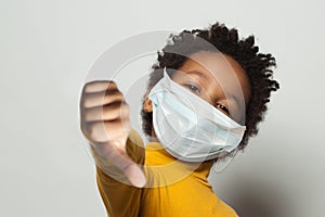 Black kid in medical protective face mask showing thumbs down on white