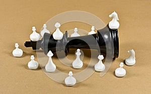 Black king chess piece fallen on a board with white small chess pieces