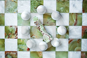 Black king fallen down, surrounded by white pawns on marble chess board from white and green marble. Business strategy with team