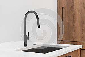 A black kitchen faucet on white marble and wood cabinets.