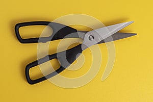 Black kitchen scissors on a yellow background.