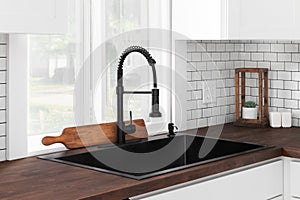 A black kitchen sink and faucet detail in a white kitchen with a butcher block countertop.
