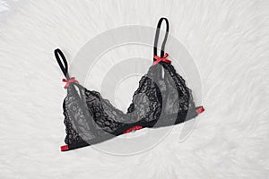 Black lace bra on white fur. Flat lay. Fashion lingerie concept