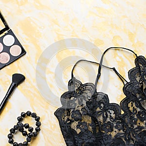 Black lace lingerie with beauty care products, make up cosmetics, jewelry in black and gold. Fashion flat lay, top view