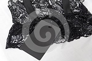 Black lace lingerie with empty black tag on white background. Transparent lace sexy bralet. Copy space