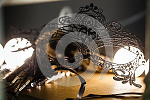 Black lace mask is on the table in a romantic atmosphere. Backlight, close-up