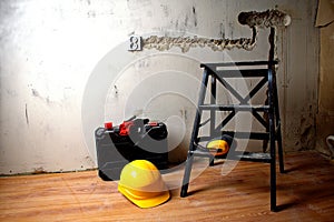 Black ladder, hard hat, ear protectors, protective gloves and tool case against the background of a concrete wall. Renovation