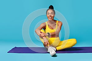 black lady in activewear with tracker sits on mat, studio
