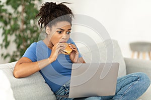 Black Lady Biting Burger Using Laptop Browsing Internet Sitting Indoor