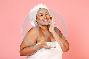 Black Lady Holding Moisturizer Applying Cream On Face, Pink Background