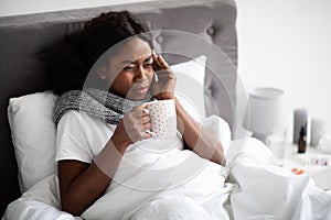 Black lady laying in bed with cup of hot drink