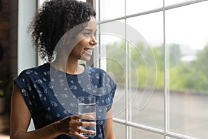 Black lady look at window holding glass of fresh aqua