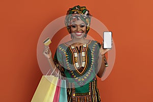 Black lady shopaholic showing smartphone and bank card