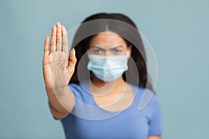 Black lady suffering from sick, wearing mask and comply with social distance, posing over blue background, studio shot. photo