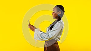 Black Lady Using Smartphone Wearing Earbuds Listening Music In Studio
