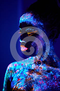 black lady with UV body art glowing in darkness, colorful prints on naked skin
