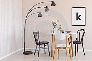 Black lamp above chairs and wooden table with flowers in dining room interior with poster. Real photo
