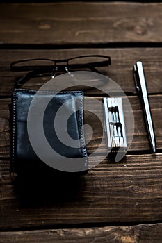 black lather wallet whit pen  eyeglasses and steel multitool on wooden table