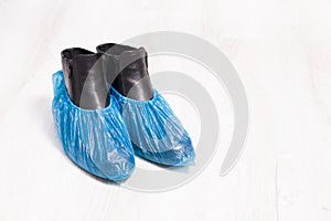 black leather boots in blue disposable shoe covers on a wooden light floor