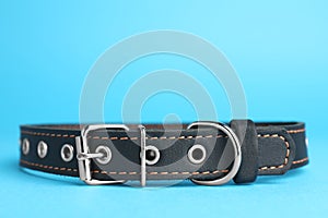 Black leather dog collar on light blue background, closeup. Space for text