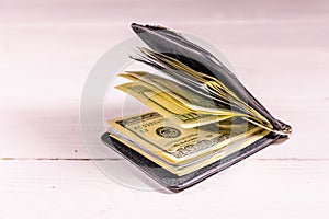 Black leather money clip with the one hundred dollar bills on wooden table