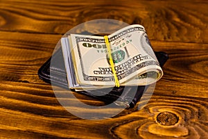 Black leather money clip with the one hundred dollar bills on wooden table