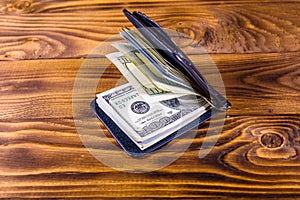 Black leather money clip with the one hundred dollar bills on wooden table