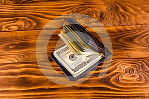 Black leather money clip with the one hundred dollar bills on wooden table