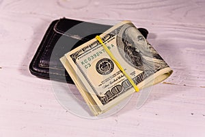 Black leather money clip with the one hundred dollar bills on wooden table
