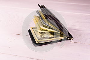 Black leather money clip with the one hundred dollar bills on wooden table