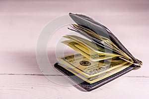 Black leather money clip with the one hundred dollar bills on wooden table