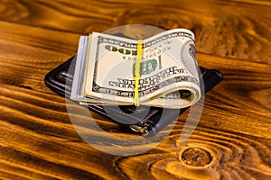 Black leather money clip with the one hundred dollar bills on wooden table