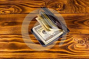 Black leather money clip with the one hundred dollar bills on wooden table